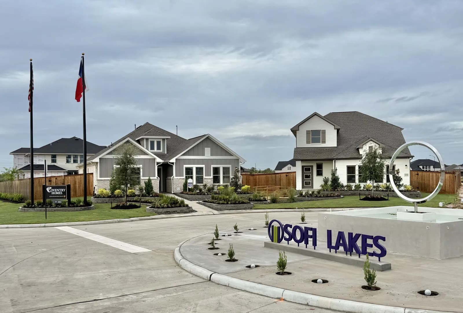 Coventry model home at Sofi Lakes in Katy, TX, with landscaped front yard, flags and the Sofi Lakes entry sign and ring sculpture in the foreground