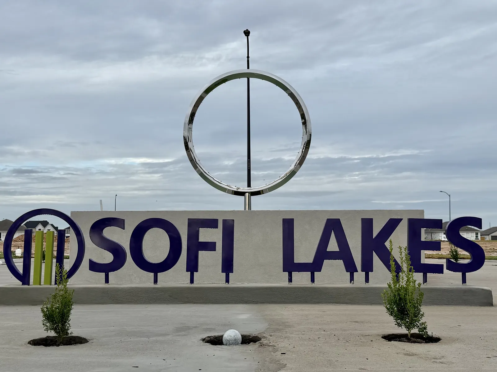 Sofi Lakes entry sign with bold purple lettering beneath a polished stainless steel ring sculpture