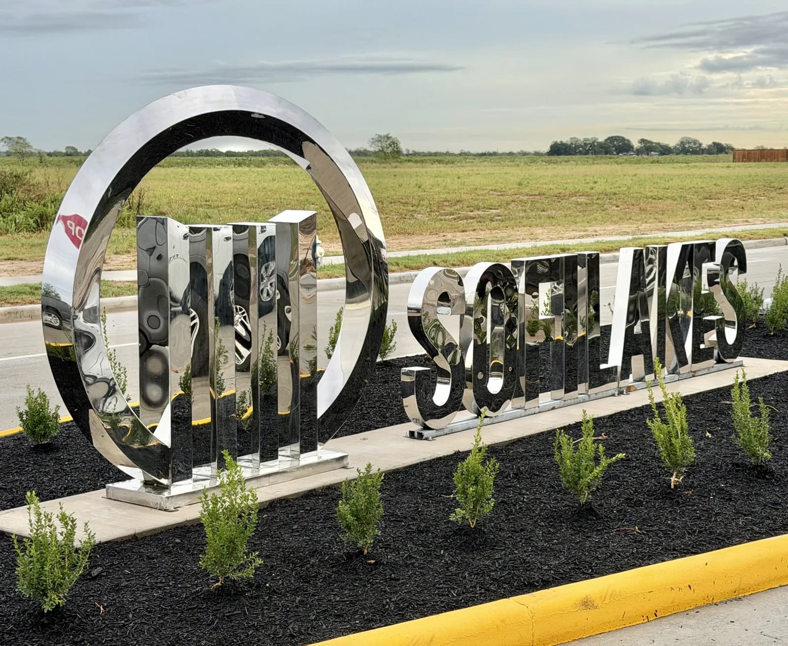Mirror-polished stainless steel Sofi Lakes monument with ring logo and lettering in a landscaped bed